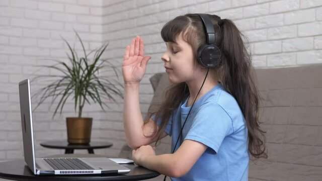 Child in headphones on online school. A little girl with a laptop and headphones raises her hand to answer. Online school concept.