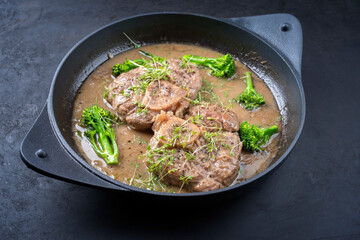 Modern style traditional braised Italian ossobuco alla Milanese with baby broccoli and herb in white wine meat sauce served in a cast-iron design skillet with copy space