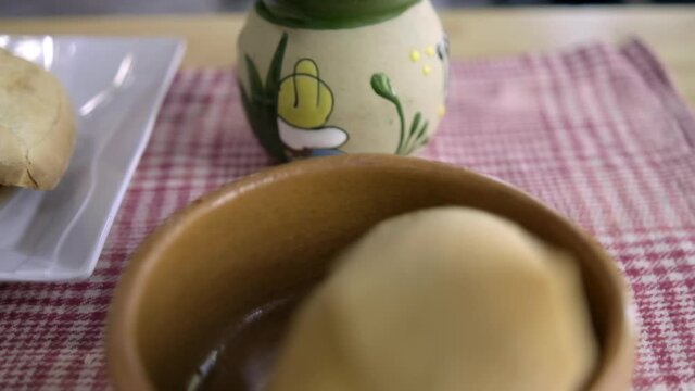 Tamale and vanilla atole in clay cups above a checkered tablecloth