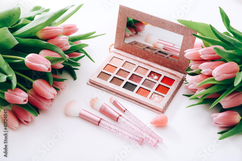 Cosmetic products for makeup and pink tulips on a light background