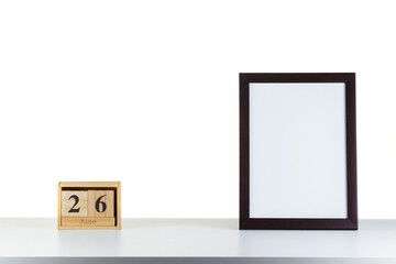 Wooden calendar 26 June with frame for photo on white table and background