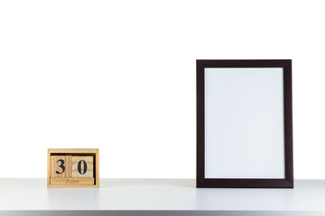 Wooden calendar 30 June with frame for photo on white table and background