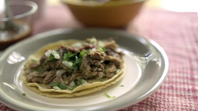Beef barbacoa taco on white plate with blurry background