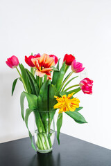 Fototapeta na wymiar Bouquet of tulips in glass vase on black table. Beautiful spring flowers. White wall. Home decor.