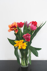Bouquet of tulips in glass vase on black table. Beautiful spring flowers. White wall. Home decor.