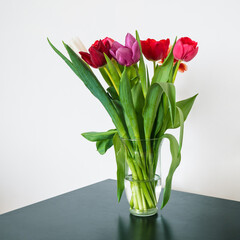 Bouquet of tulips in glass vase on black table. Beautiful spring flowers. White wall. Home decor.