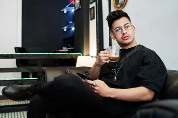 boy dressed in black sits drinking coffee while waiting for his turn in a barber shop