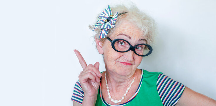 Old wrinkled hipster woman in glasses points her finger to the ad spaces with a emotional face. Elderly woman in stylish clothes. Advertising space. Copyspace