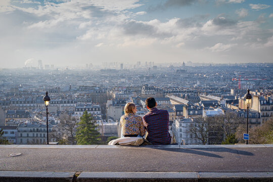 Paris, France - 02 26 2021: Montmartre district. View of Paris from square Louise Michel and a young couple sitting on the steps