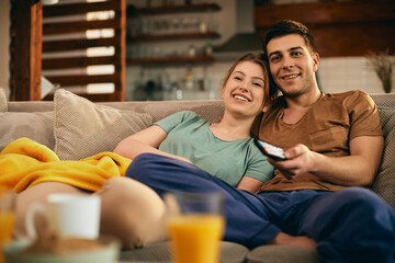 Happy couple watching movie while relaxing on the sofa at home.