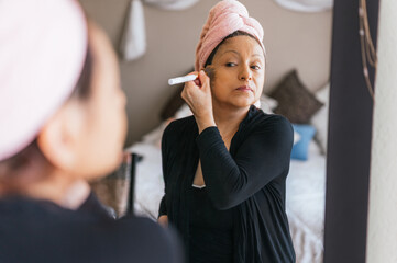 Portrait of a 40-year-old woman applying makeup in front of a mirror