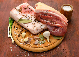 raw pork meat and lard with salt, spices and garlic on a cutting board, dark wooden background