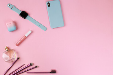 Smart gadgets on pink background. Phone, headphones, smart watch and lip gloss, perfume and makeup brushes. Top view with copy space, flat lay. Woman devices