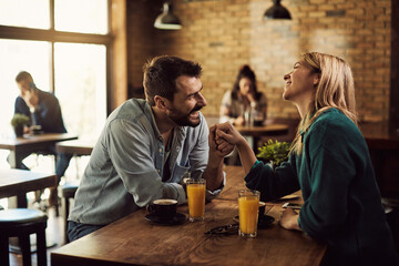 Happy couple holing hands while talking in a cafe.