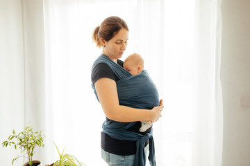 Happy mother with sleeping newborn in baby carrier