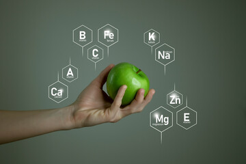 Woman`s hand holding green apple, microelement icons in molecular hexagons on grey background....