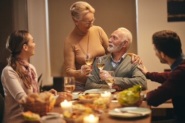 Mature couple toasting with wine while having dinner with their adult children at home.