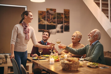 Happy woman toasting with her family while having dinner at dining table.