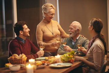 Happy senior woman toasting with her family during a meal at dining table.