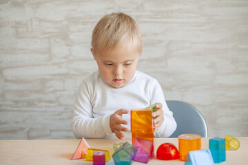 Little cute boys with a genetic disease are sitting at the table. Reenok with Down Syndrome plays...