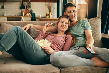 Smiling couple eating popcorn and watching TV while relaxing on the sofa.