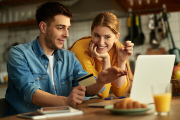 Happy couple using credit card and laptop while shopping on the internet at home.