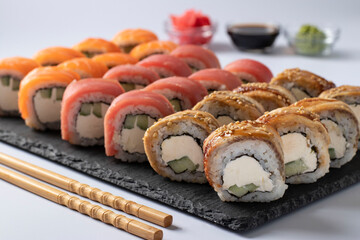 Asian food with sushi set of salmon, tuna and eel with philadelphia cheese on a slate board on a white background. Served with soy sauce, wasabi and pickled ginger. Closeup.