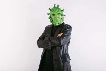Person disguised as coronavirus with latex mask - covid-19 virus, wearing black leather frock coat and black t-shirt, with crossed arms, on white background. Coronavirus concept