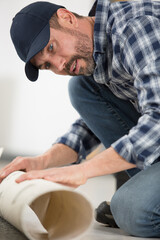 male worker unrolling carpet on floor at home