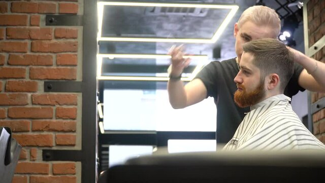 A young man with a beard is sitting in a hairdresser's chair during a haircut. Side view