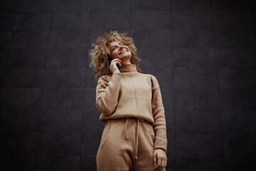 Low angle view of smiling trap girl in tracksuit standing and having phone call with a friend.