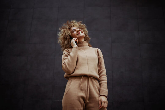 Low angle view of smiling trap girl in tracksuit standing and having phone call with a friend.