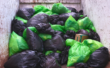 dumpster full of black and green garbage bags
