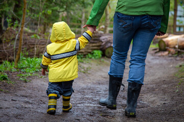 Mother and toddler going for a walk on a muddy trail wearing boots and raincoats