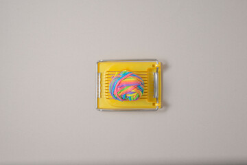 Yellow egg slicer with multicolored rubber bands on a gray background