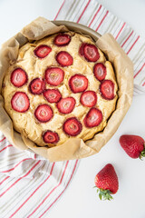 Strawberry cake on a red and gray striped tea towel in vertical orientation with two strawberries on the side.