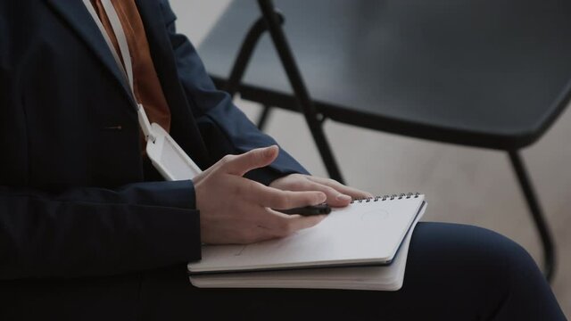 Steadicam of cropped unrecognizable business person in formal suit, sitting, fumbling pen in hand over notebook