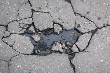 Obraz premium Large cracks on asphalt road filled with water, damage to the road surface in spring