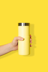 Hand holds yellow travel mug isolated on white background. Thermo cup or tumbler in female hand