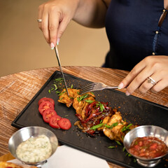 Woman having lunch in restaurant. Close up shot of female hands with knife, fork and Food plate, Side view. Appetizer dish from restaraunt menu. Exquisite served dish. Square format.