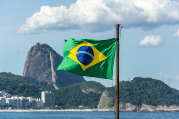 Brazilian flag at Copacabana Beach backlit by golden sunrise view of Sugarloaf Mountain in Rio de Janeiro Brazil