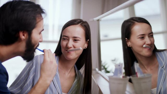 Young couple brushing teeth in front of mirror indoors at home.