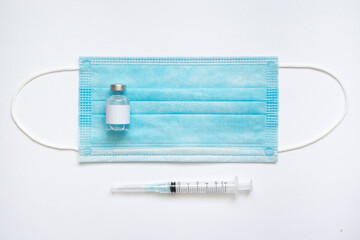 Medical vial of injectable medicine and hypodermic needle on a blue mask