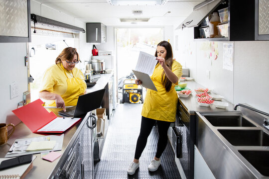 Food truck owner and worker checking stock list with laptop
