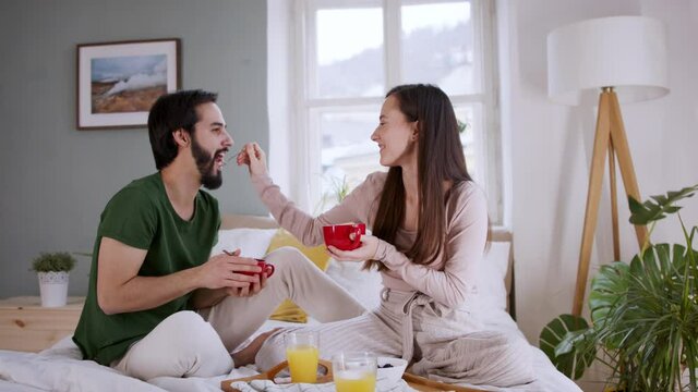 Young couple in love eating breakfast on bed indoors at home.