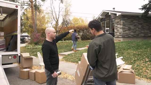 Man Guiding Movers With Boxes Outside New House