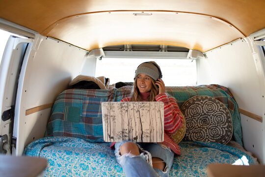 Carefree young woman with headphones and laptop in camper van