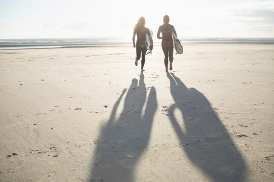 Female surfers running with surfboards on sunny idyllic beach