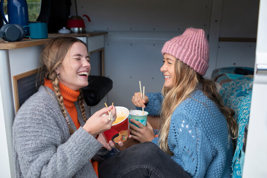 Happy young women friends eating instant noodles in camper van
