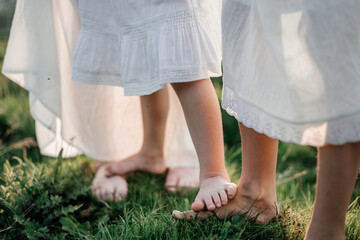 Barefooted little girls and mother stand on green grass